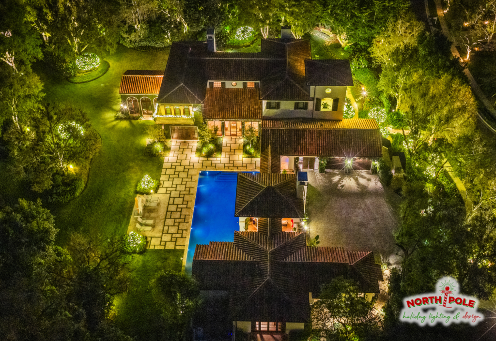 Aerial view of a luxury Palm Beach estate with automated holiday lighting, pool accents, and lit tree canopies.