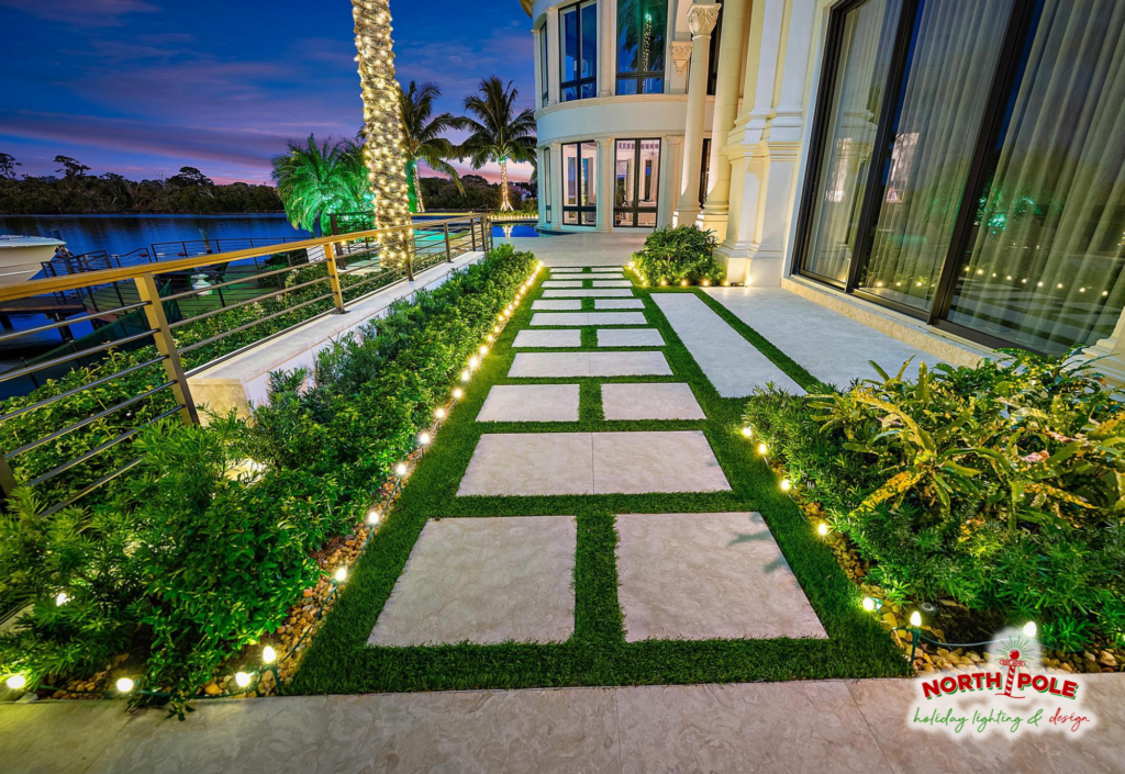 Modern waterfront estate in BallenIsles Palm Beach Gardens featuring holiday pathway lighting and warm white LED palm tree wraps.