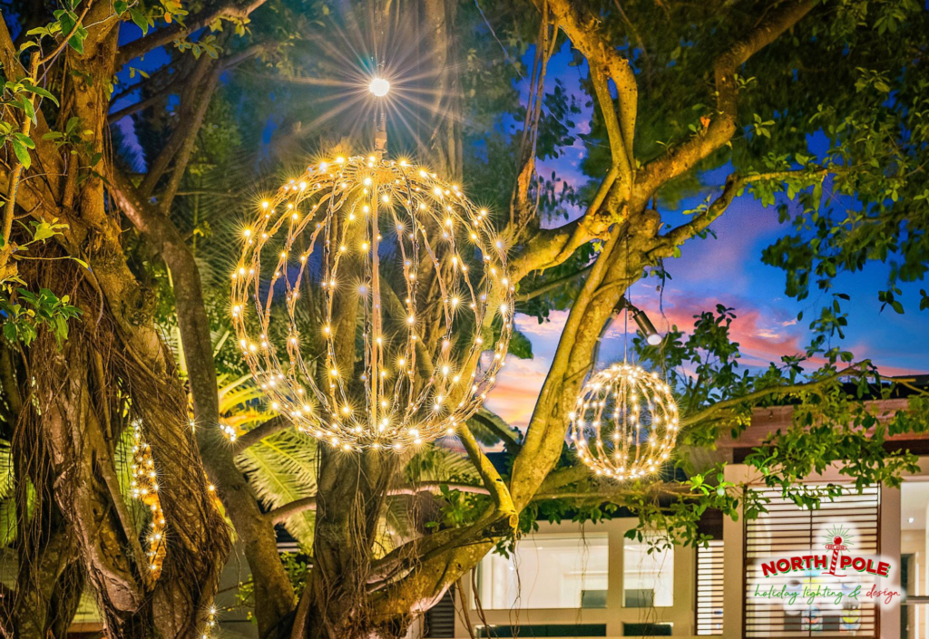 Close-up of premium warm white LED light spheres installed in lush green foliage at a luxury Palm Beach estate, showing professional rigging.