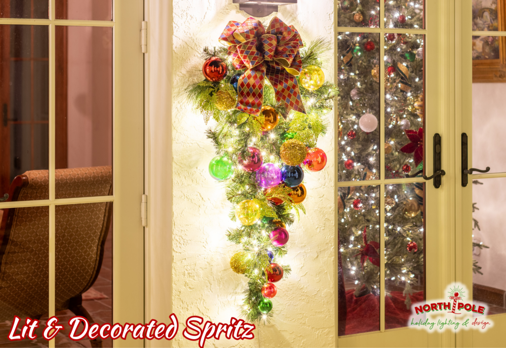 Decorative holiday spritz greenery with ornaments and warm white lights installed on a luxury home in Palm City.