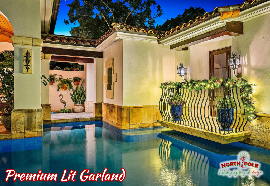 Professional holiday garland with warm white lights installed on a luxury pool deck railing in Tequesta.