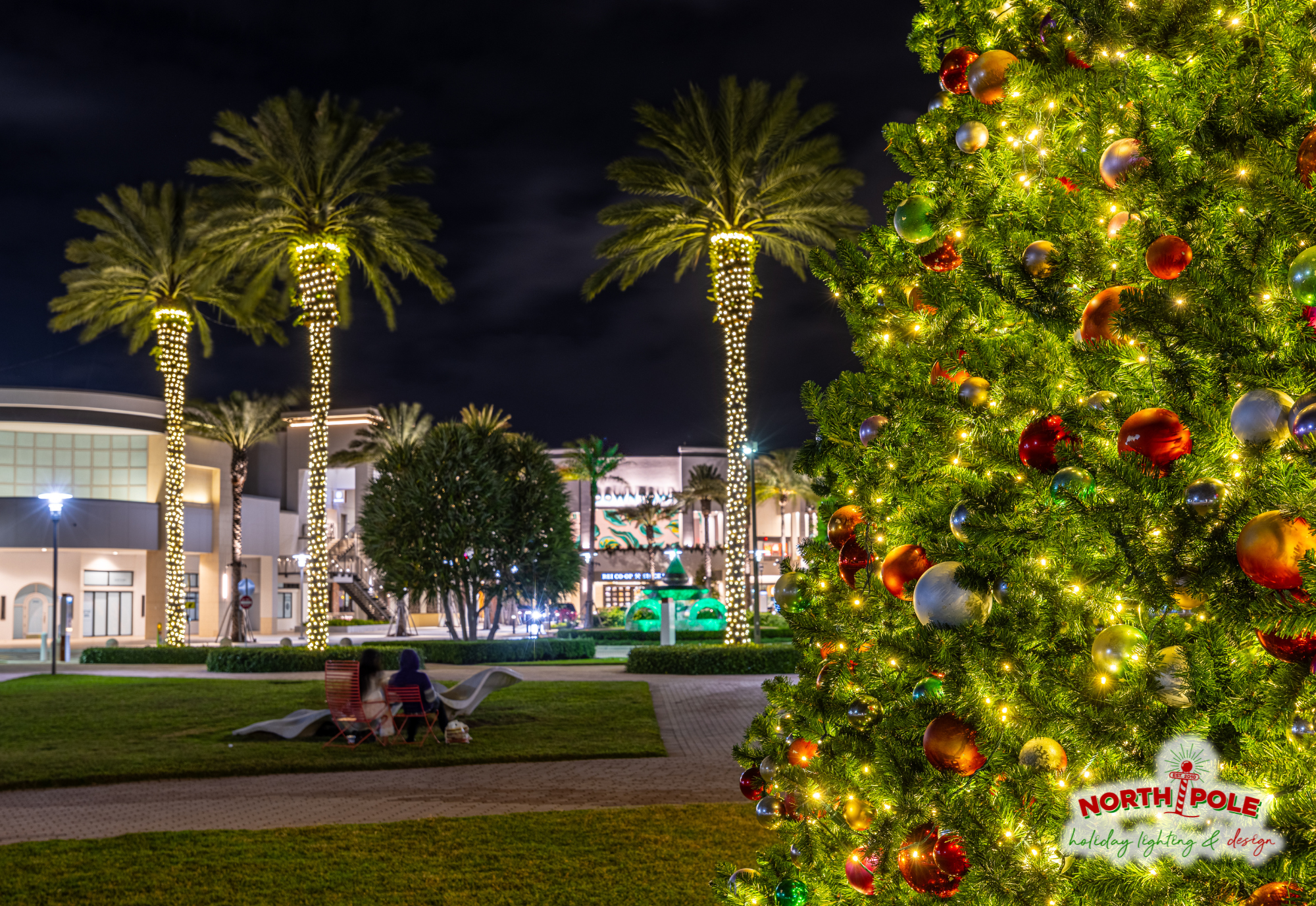 Detail shot of decorated commercial Christmas tree branch with shatterproof ornaments and warm white LED palm wraps, installed at Downtown Palm Beach Gardens.