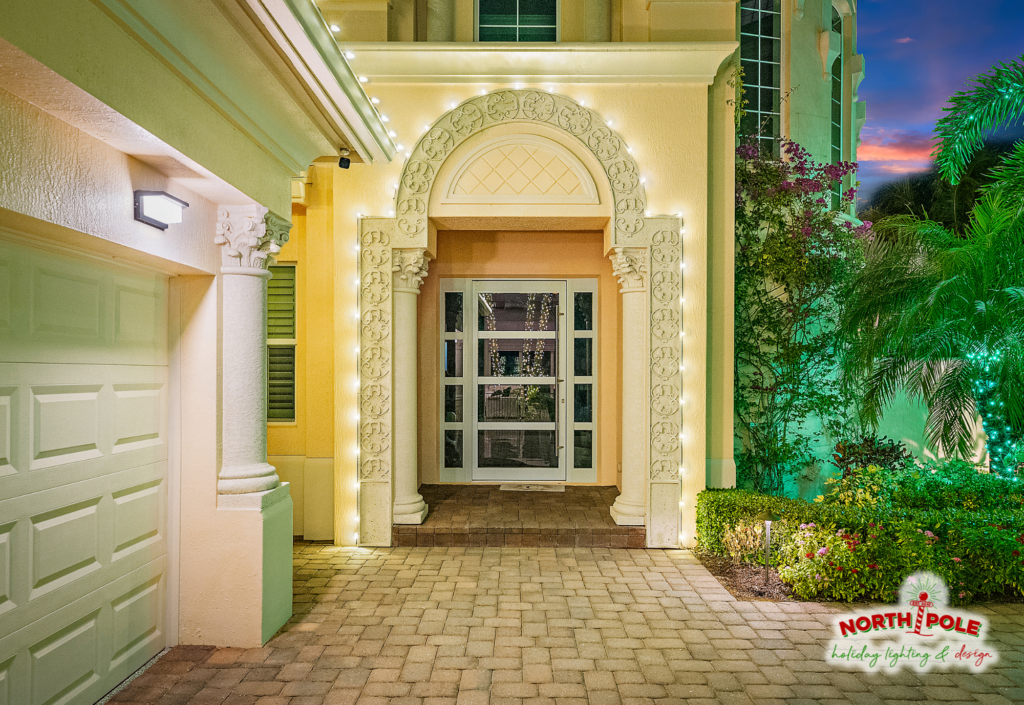 Close-up of warm white LED holiday roofline lighting custom-fitted to an ornate arched entryway on a luxury Florida home.